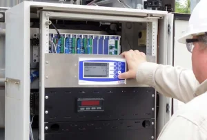 A person's hand touches a digital control panel inside an open electrical cabinet.