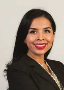 A smiling woman with long dark hair wears a black blazer and a patterned shirt.