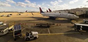 A Delta airplane sits on an airport tarmac near ground service vehicles.