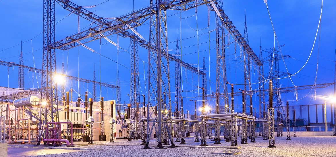 An electrical substation with metal towers and power lines under a blue sky.