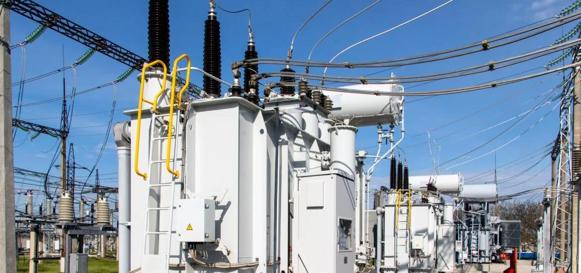 Large electrical transformers and power lines stand under a blue sky.
