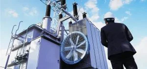 A person in a hard hat stands next to a large electrical transformer.
