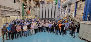 A large group of people in hard hats stands in an industrial facility.