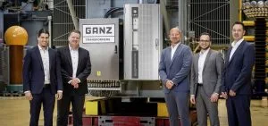 Four men in suits stand in front of a large industrial transformer.