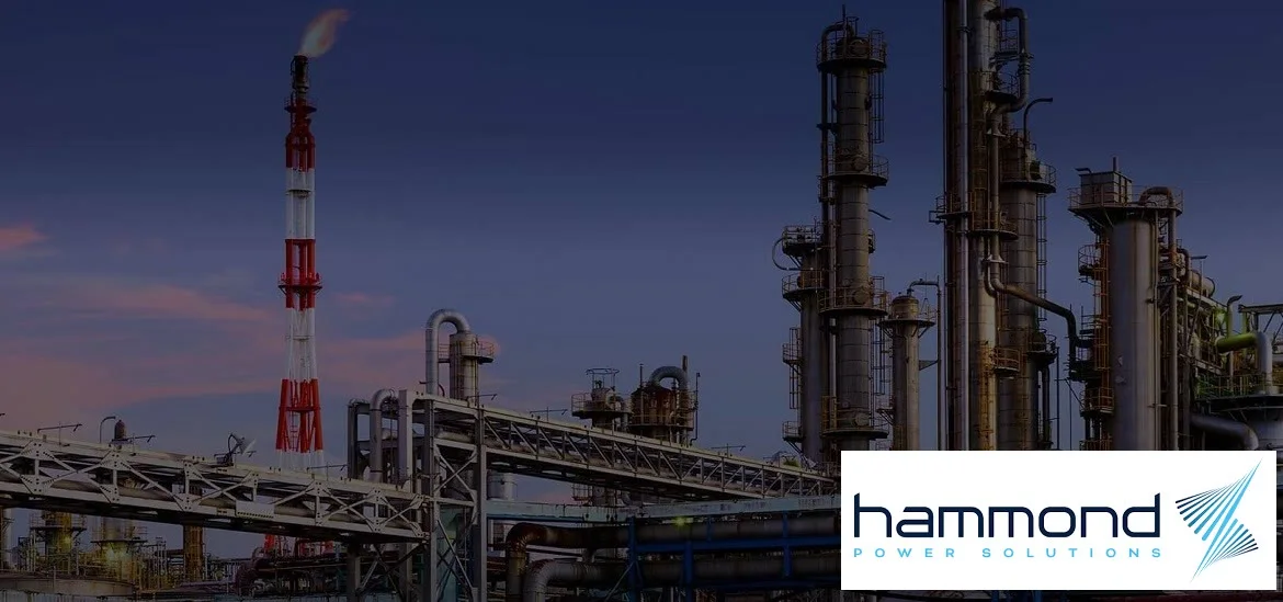 Industrial refinery towers and pipes stand against a twilight sky.