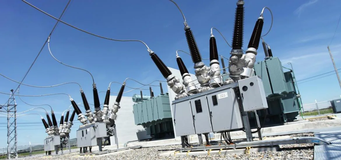 Electrical transformers stand in an outdoor substation under a blue sky.