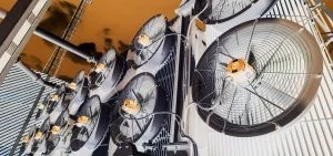 Large industrial cooling fans are mounted on a white structure against an orange sky.