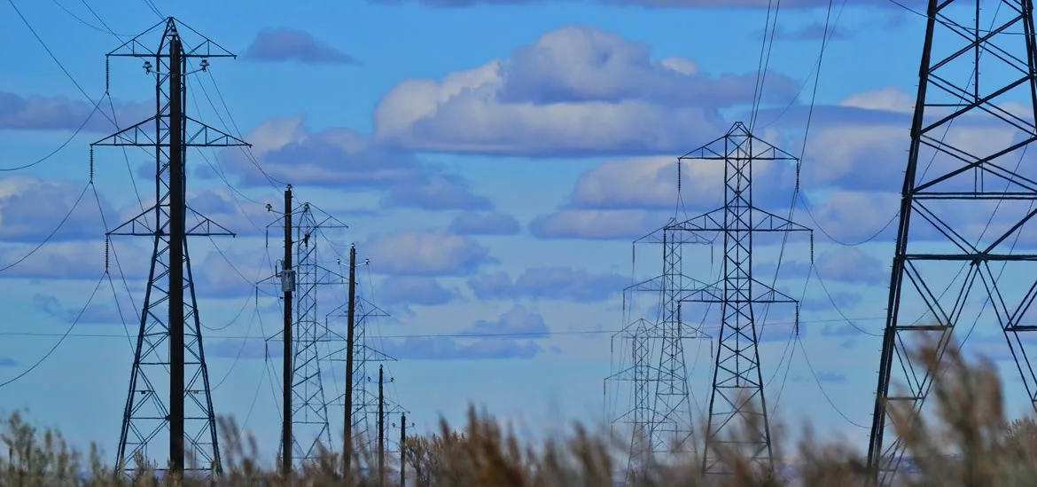 Several electrical transmission towers stand against a blue sky with clouds.