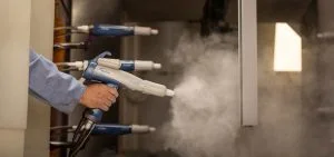 A person holds a spray gun that is emitting a white mist.