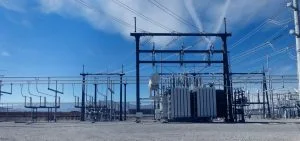 An electrical substation stands under a blue sky with wispy clouds.