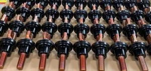 Rows of black cylindrical components with copper-colored metal rods are arranged on a surface.