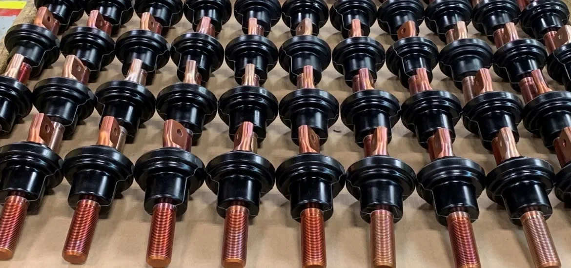 Rows of black cylindrical components with copper-colored metal rods are arranged on a surface.