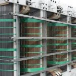 A large industrial electrical transformer with visible copper coils and metal framing.