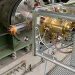 A metal device with a screen and various wires is attached to a large industrial machine.