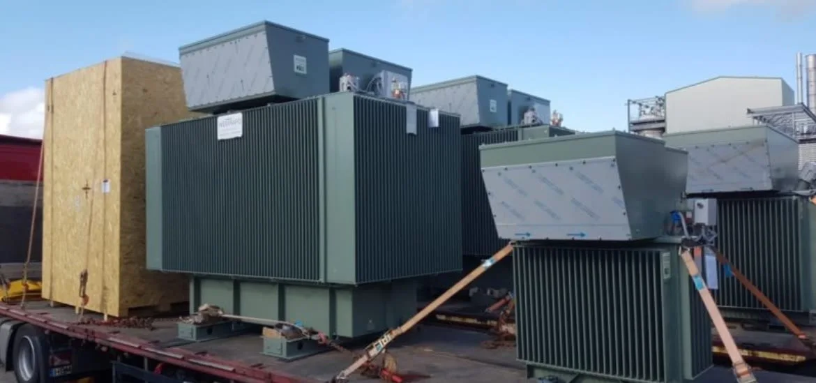 Large green industrial electrical transformers sit on a flatbed truck.