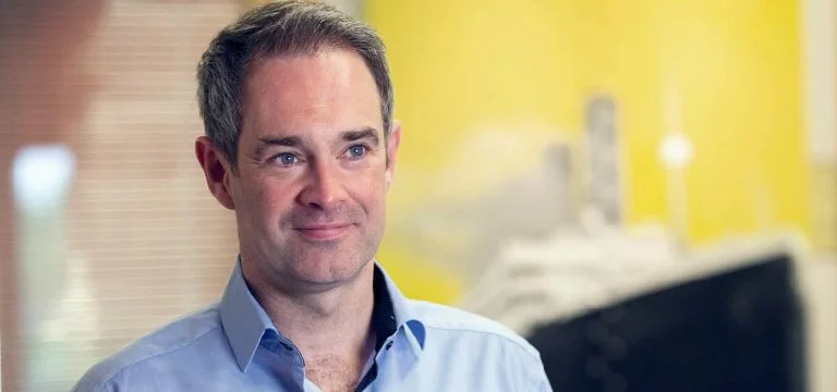 A man in a light blue collared shirt looks to the side.