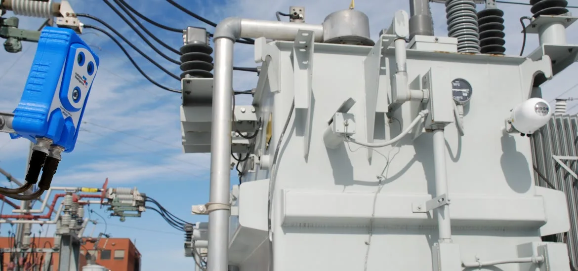 A large grey electrical transformer sits under a blue sky.