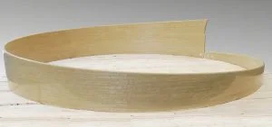 A shallow, circular wooden tray sits on a light-colored wooden surface.