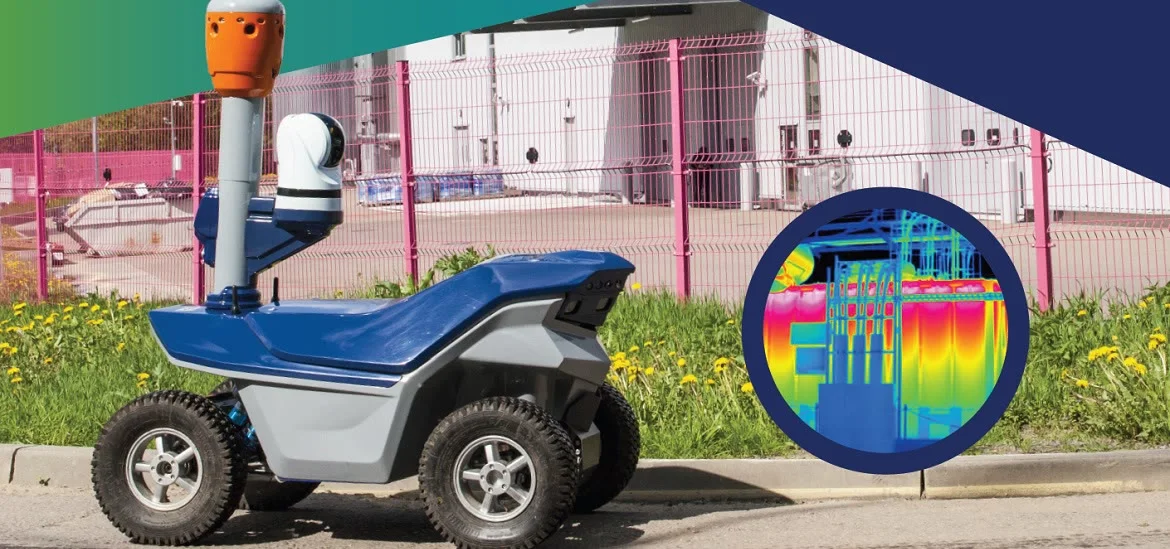 A small blue and grey robotic vehicle sits on a paved surface next to a pink fence.