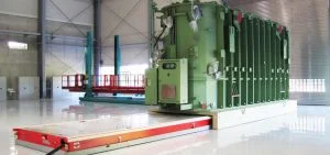A large green industrial machine sits on a white platform in a warehouse.