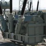 A large grey electrical transformer sits on a gravel ground.