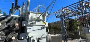 Large electrical transformers and power lines stand under a clear blue sky.