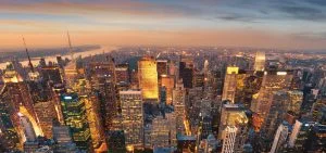 An aerial view of a city skyline at sunset with illuminated skyscrapers.