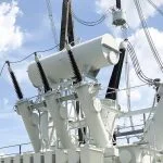 White electrical transformers stand against a cloudy sky.