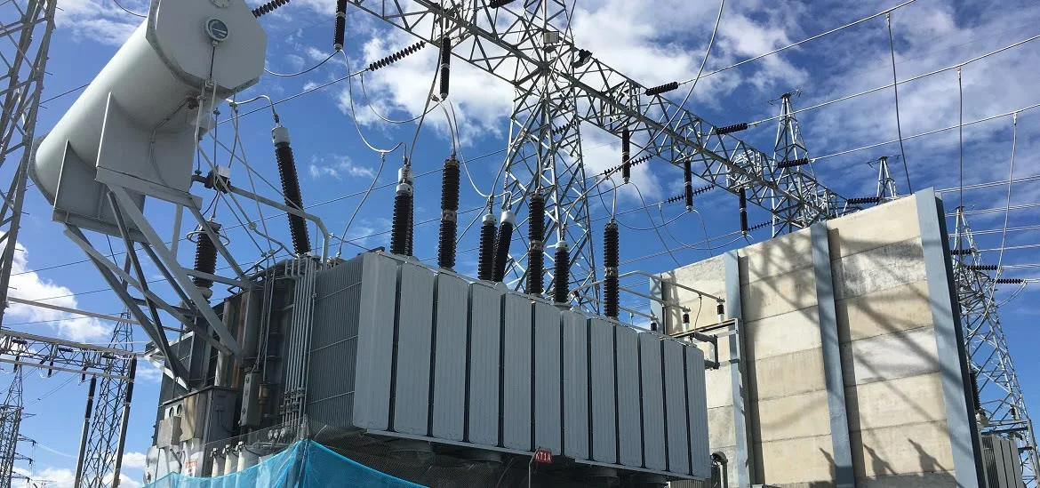 Electrical transformers and power lines stand against a blue sky with clouds.