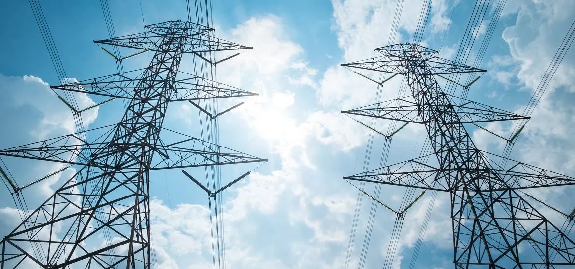 Two electrical transmission towers stand against a blue sky with clouds.