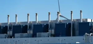 Several silver exhaust pipes stand on top of a blue and gray industrial building.