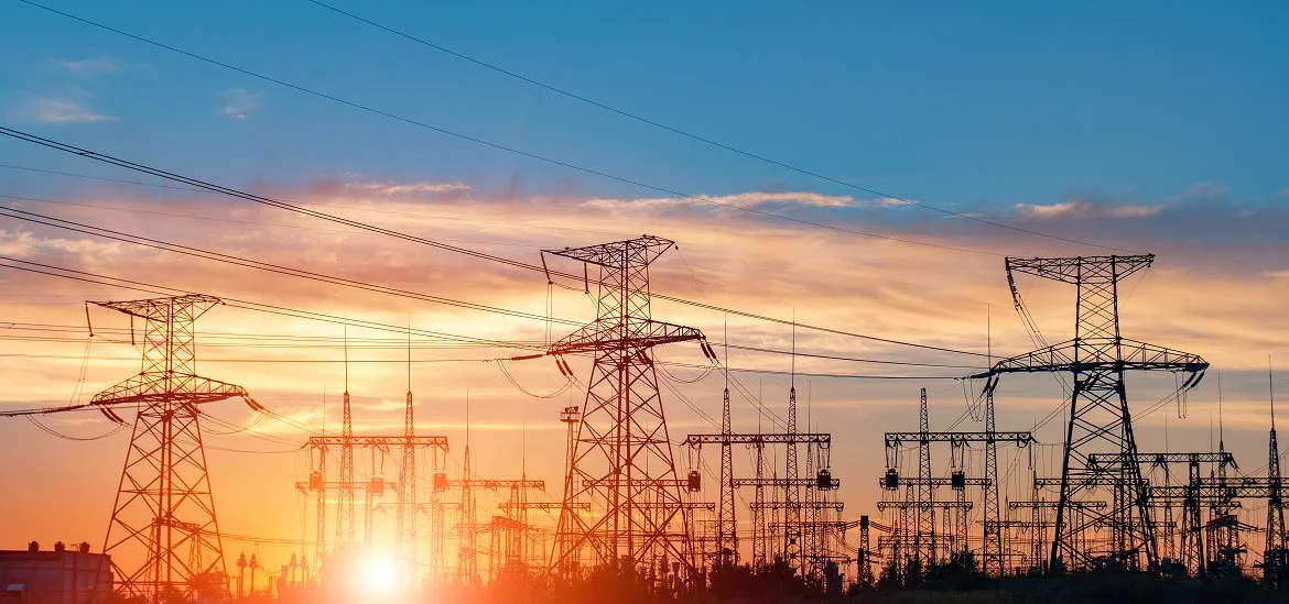 Electrical transmission towers stand against a sunset sky.