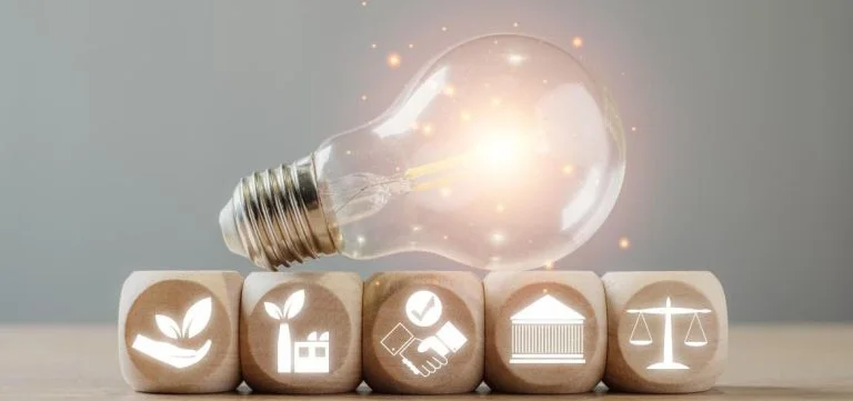 A glowing light bulb rests on a row of wooden blocks with white icons.