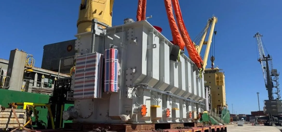 A large gray industrial machine sits on a flatbed trailer under a clear blue sky.