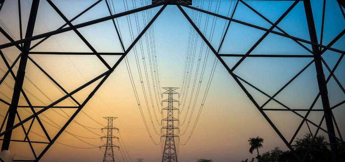 Power lines and transmission towers stand against a sunset sky framed by a metal structure.