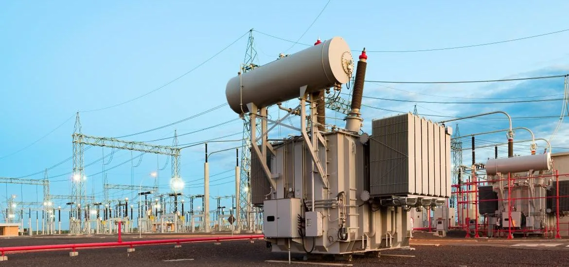 An electrical transformer stands in an outdoor substation under a clear sky.