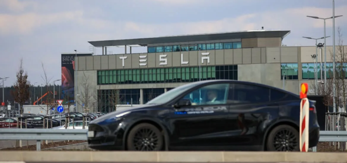 A black car drives past a building with the word "TESLA" on it.