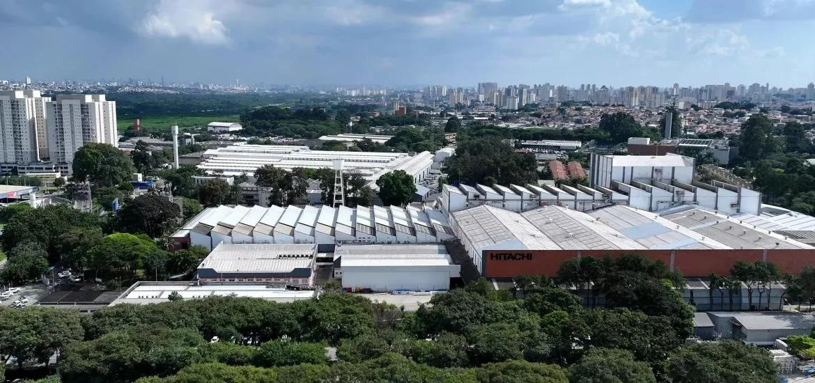 An aerial view of industrial buildings and a city skyline under a cloudy sky.