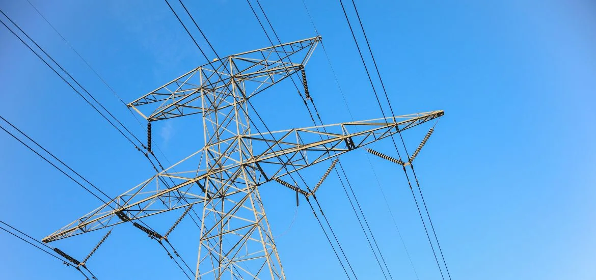 An electricity pylon stands against a clear blue sky with power lines attached.