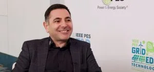 A man in a dark shirt and blazer smiles.