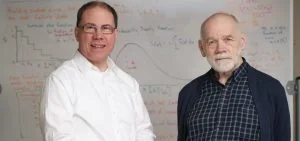 Two men stand in front of a whiteboard covered in mathematical equations.