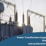 Electrical transformers and power lines stand under a bright sky.