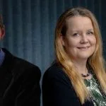A man and a woman smile against a dark, textured background.