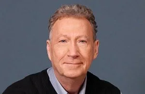 A man with light skin and wavy hair smiles at the camera.