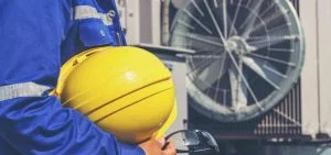 A person in blue workwear holds a yellow hard hat.