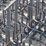 Electrical insulators and metal structures stand on a gravel ground.