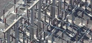 Electrical insulators and metal structures stand on a gravel ground.