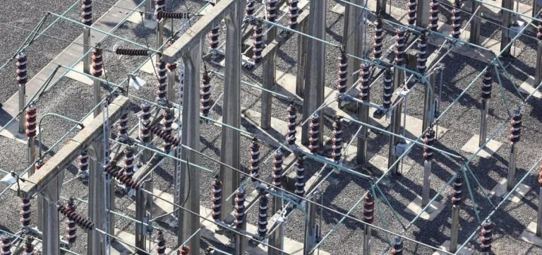 Electrical insulators and metal structures stand on a gravel ground.