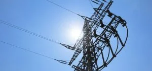 An electrical transmission tower stands against a clear blue sky with the sun shining through the structure.