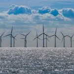 Wind turbines stand in the ocean under a cloudy sky.